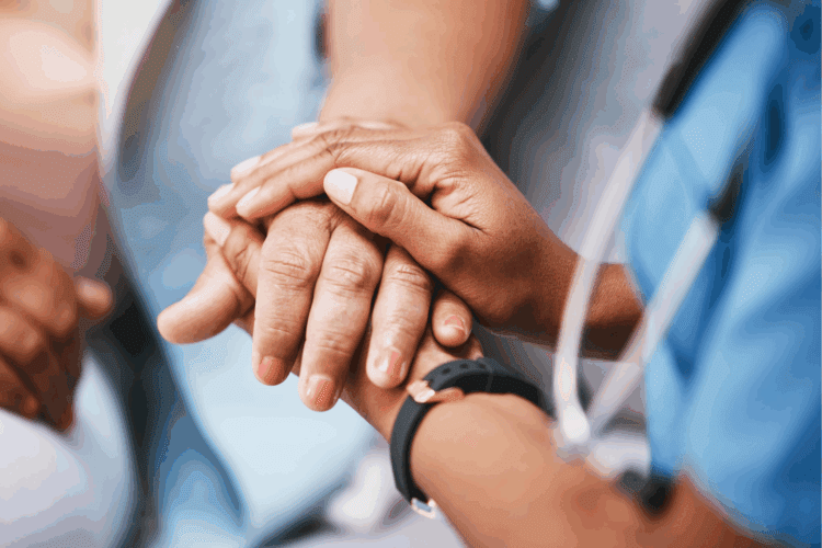Close-up of a healthcare worker’s hand gently holding a patient’s hand, conveying comfort and support.