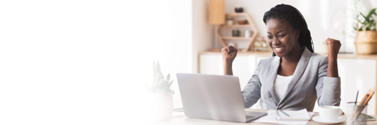 A woman in business attire smiles and raises her fists in excitement while sitting at a desk with a laptop, notebook, and coffee cup—celebrating successful AP automation ERP integration.