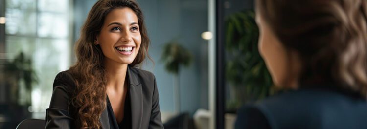 Two women sit across from each other in a modern office, smiling and engaged in conversation—perhaps discussing onbase workday integration during a professional meeting or interview.
