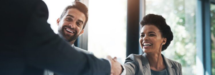 Two professionally dressed people, a man and a woman, smiling and shaking hands with another person in a bright office setting—debunking common HR automation myths through genuine human connection.