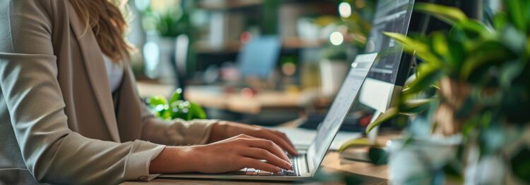 A person types on a laptop at a desk surrounded by green plants in a modern, well-lit office, enjoying hr technology savings in an inspiring workspace.