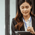 A woman in business attire uses a digital tablet and stylus while sitting at a desk with a laptop, embracing 2025 HR trends in a modern office setting.