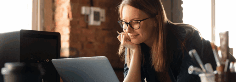A woman wearing glasses sits at a desk, smiling at her laptop screen as she researches what is a website accessibility rating, with a coffee cup and office supplies nearby.