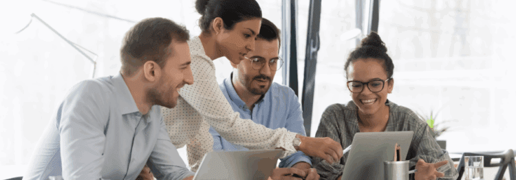 Four people sit at a table in an office, collaborating and looking at laptops as one person explains an intelligent document processing definition on the screen.