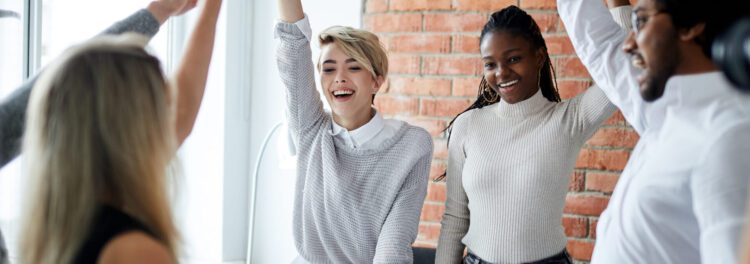 Four people in casual office attire smile and raise their arms in a bright, modern workspace with a brick wall background, celebrating accounts payable growth.