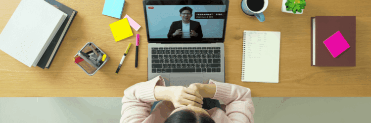A person sits at a desk watching a webinar on a laptop, surrounded by stationery, a notebook, sticky notes, a potted plant, and a cup of coffee, focused on upskilling and reskilling for career growth.