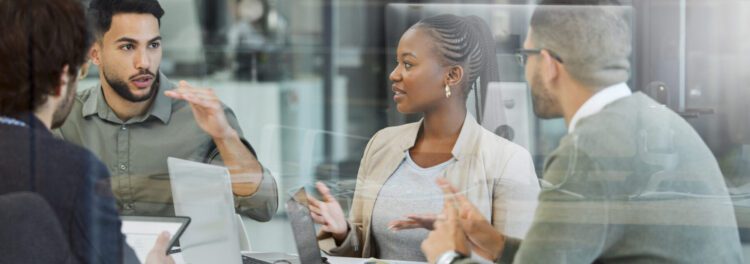 Four people are sitting at a table in an office, engaged in a discussion about cloud enablement with laptops and documents in front of them.