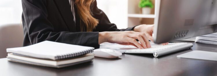 Person in business attire typing on a keyboard at a desk with a stack of notebooks, computer mouse, and monitor—focused on implementing data conversion best practices for efficient workflow.