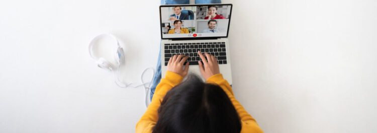 Person in a yellow sweater using a laptop for a video call with four people; headphones rest beside them on a white surface, reflecting the role of digital transformation in enhancing the employee experience.