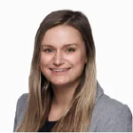 A woman with long, straight, light brown hair smiles at the camera. She is wearing a gray blazer over a black top, posed in front of a plain white background.
