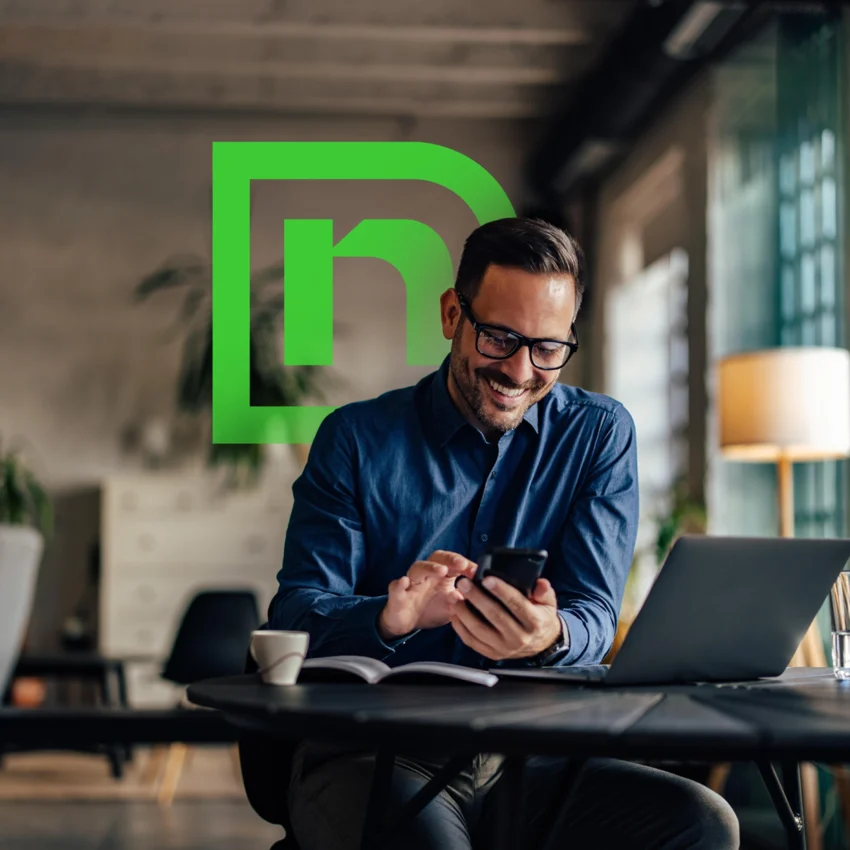 A man sits at a desk using his smartphone and laptop, smiling, with a green stylized "n" logo in the background.
