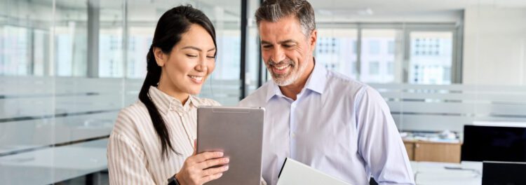 Two colleagues stand in an office, smiling as they explore automation use cases together on a tablet.