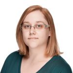 A woman with straight, shoulder-length light brown hair, wearing glasses and a teal top, poses against a plain white background.