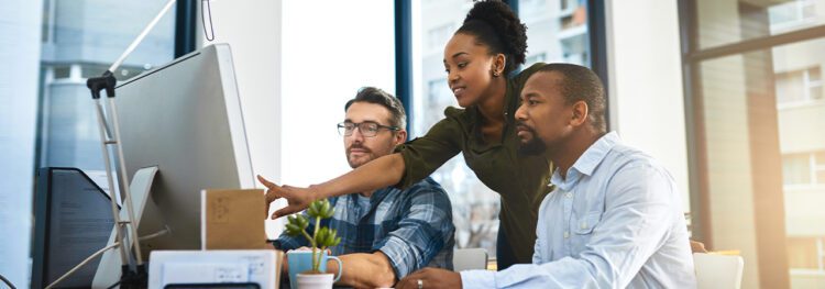 Three people in an office look at a computer monitor together, discussing intelligent document processing benefits as one person points at the screen while the others watch attentively.
