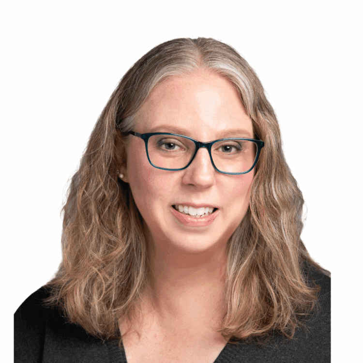 Woman with shoulder-length wavy gray hair, wearing blue glasses and a black top, smiling at the camera against a plain white background.