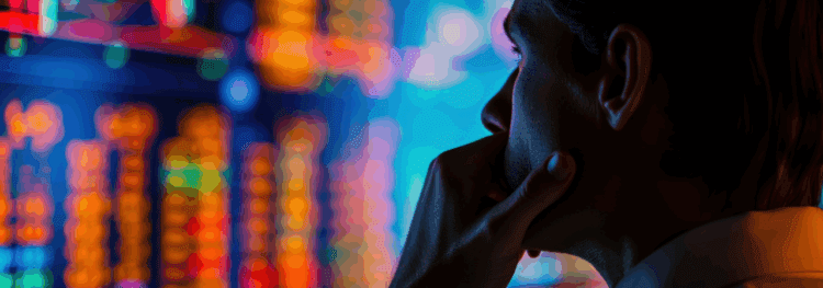 A person looks thoughtfully at colorful, blurred financial or stock market data on a large screen, contemplating what is process intelligence in the context of modern analytics.