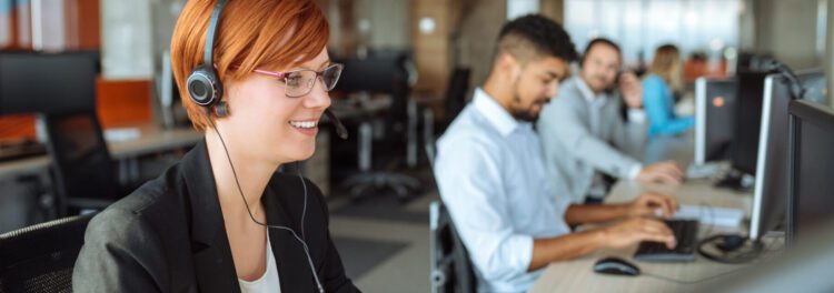 Several people are seated at desks in a modern office, wearing headsets and working on computers as they discuss Hyland cloud tips to boost productivity.