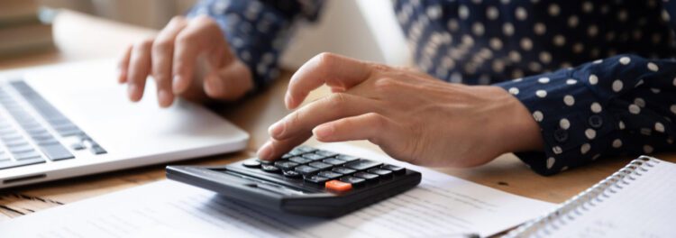 Person using a calculator and laptop at a desk with papers and a notebook, focusing on calculations or financial work—possibly integrating ap automation software for streamlined processes.