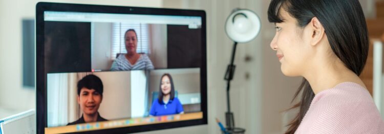 Woman sits at a desk in front of a computer, participating in a remote RPA video call with three other people shown on the monitor.