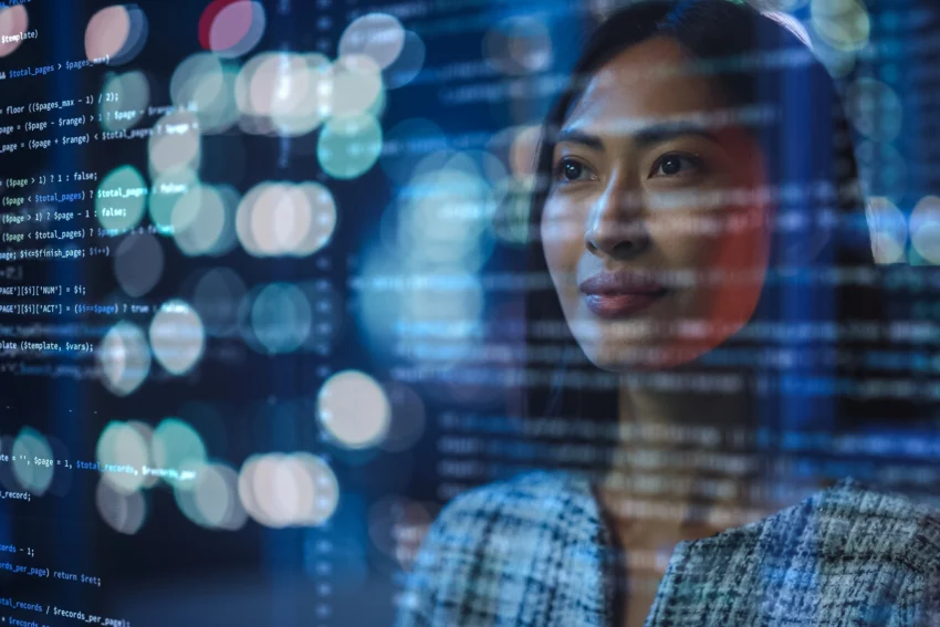 A woman looks through a transparent screen displaying lines of computer code, with city lights blurred in the background.
