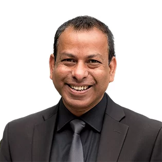 Man wearing a black suit, black shirt, and black tie, smiling at the camera against a white background.