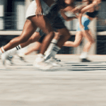A group of people in athletic wear are sprinting outdoors, with motion blur highlighting their fast movement.