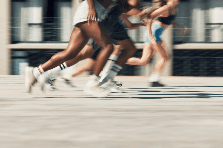 A group of people in athletic wear are sprinting outdoors, with motion blur highlighting their fast movement.