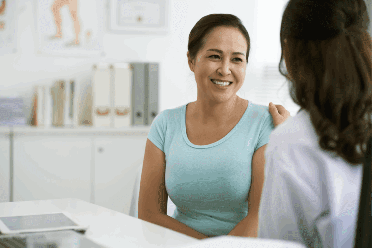 A woman in a light blue shirt smiles while speaking with a medical professional in an office setting.