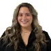 A person with long wavy hair wearing a black shirt is smiling at the camera against a white background.