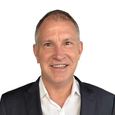 Smiling middle-aged man in a white shirt and dark blazer, with short hair, posing against a plain white background.