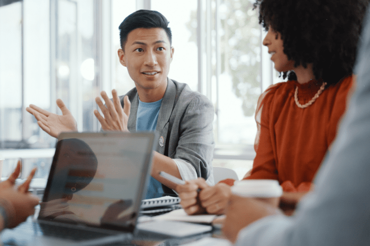 A group of people sit around a table in a bright office, discussing content‑centric intelligent automation with a laptop and notebooks in front of them.