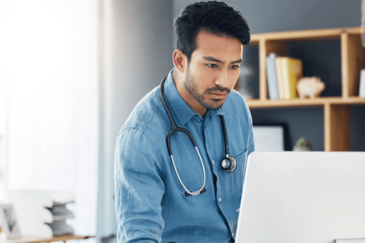 A male doctor with a stethoscope around his neck looks at a computer screen in a modern office, utilizing intelligent automation healthcare for enhanced patient care.