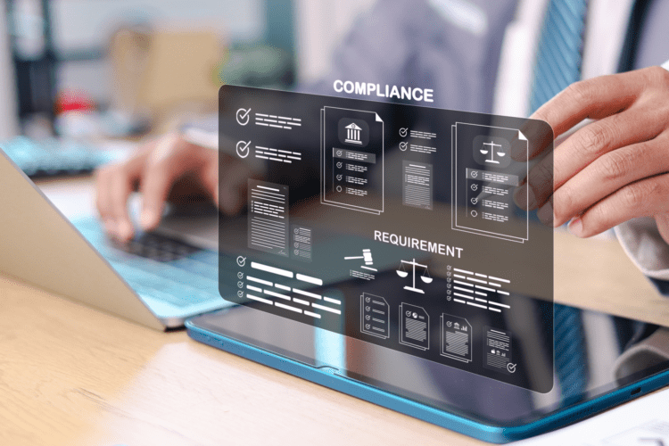 A person in business attire types on a laptop, with digital graphics labeled "Compliance" and "Requirement" displayed on a transparent screen above the keyboard.