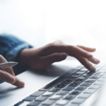 Close-up of a person’s hands using a laptop keyboard, with one hand holding a digital stylus—illustrating modern work environments driven by AI in claims processing and innovative claims automation ROI solutions.
