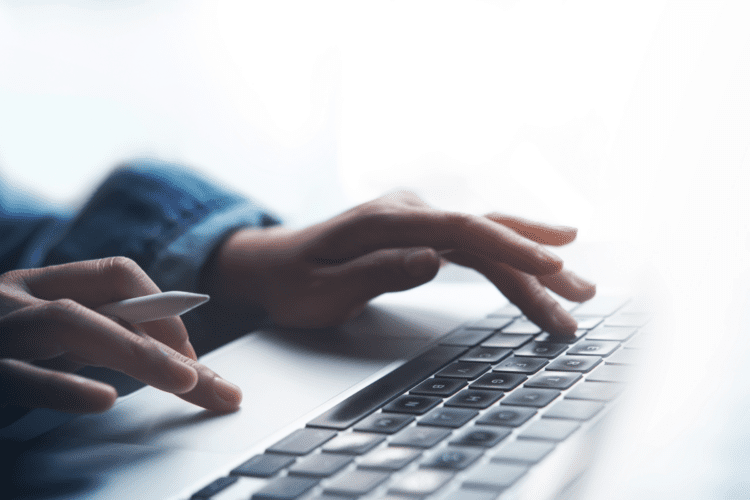Close-up of a person’s hands using a laptop keyboard, with one hand holding a digital stylus—illustrating modern work environments driven by AI in claims processing and innovative claims automation ROI solutions.