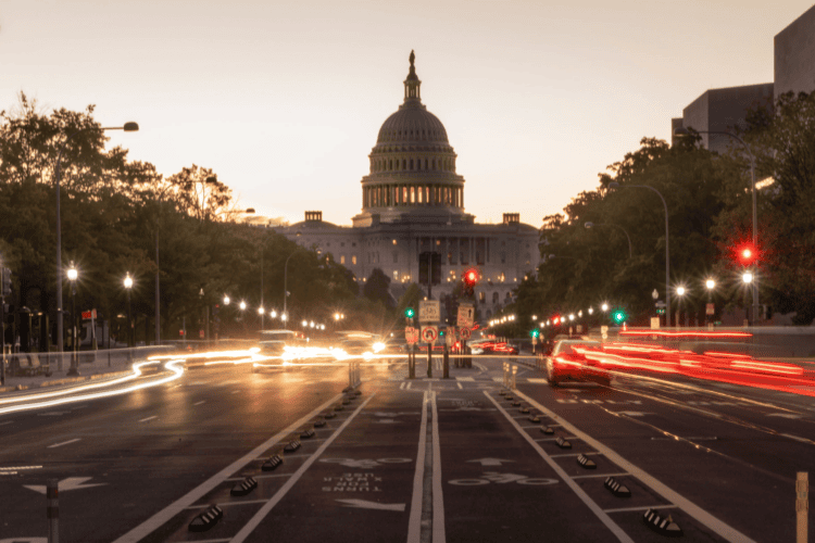 The U.S. Capitol building at dusk with blurred car lights on a street in the foreground and bike lanes visible in the center—a powerful reminder of civic progress that prompts reflection on why government AI projects fail without an effective enterprise knowledge layer to unify efforts.