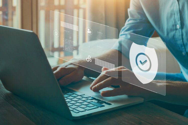 Person typing on a laptop with digital security icons and a shield symbol overlayed, representing cybersecurity and data protection.